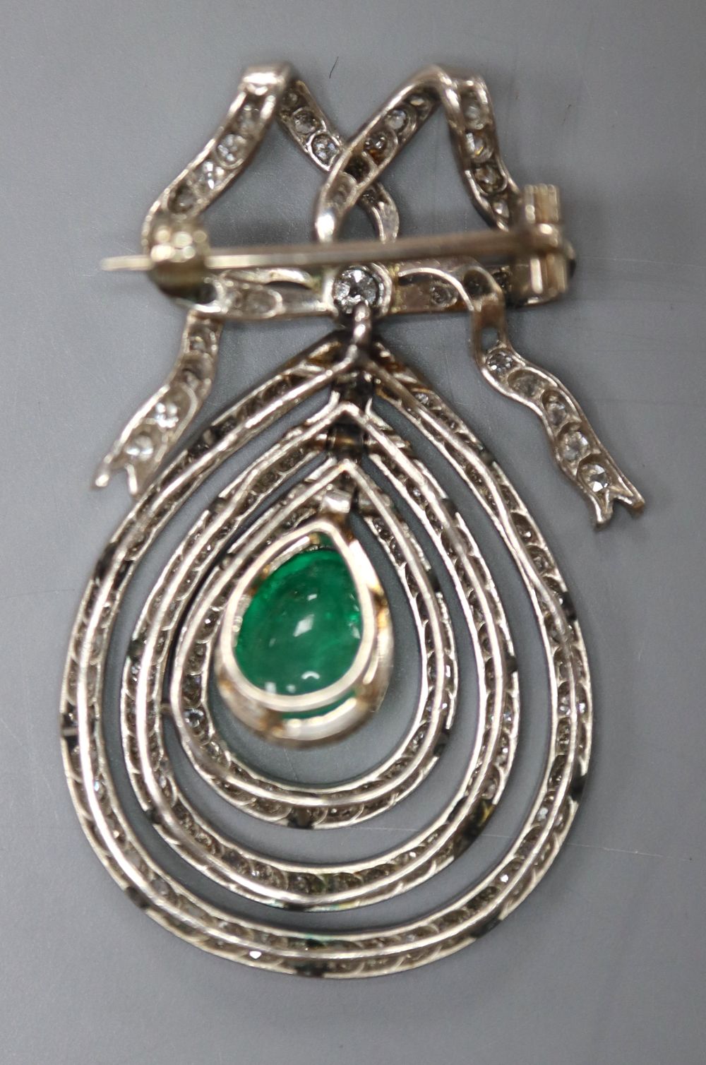 An Edwardian articulated white metal, cabochon emerald and diamond set teardrop shaped drop brooch,
